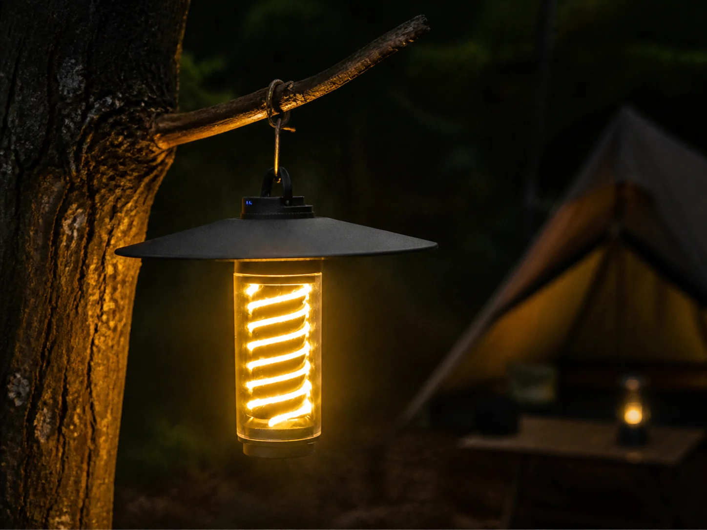 Black ambient camping tower light hanging from a tree branch at a campsite